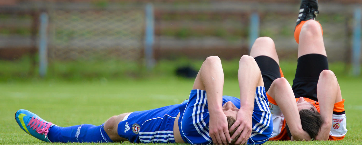 Two teens lying on the ground holding their heads