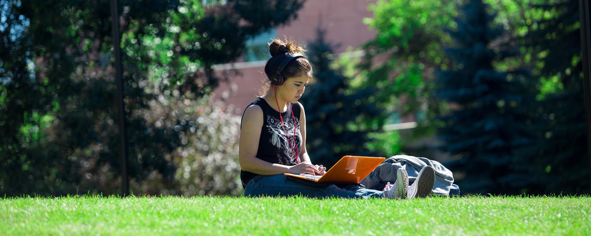 Student sitting with her laptop on the grounds of UCalgary