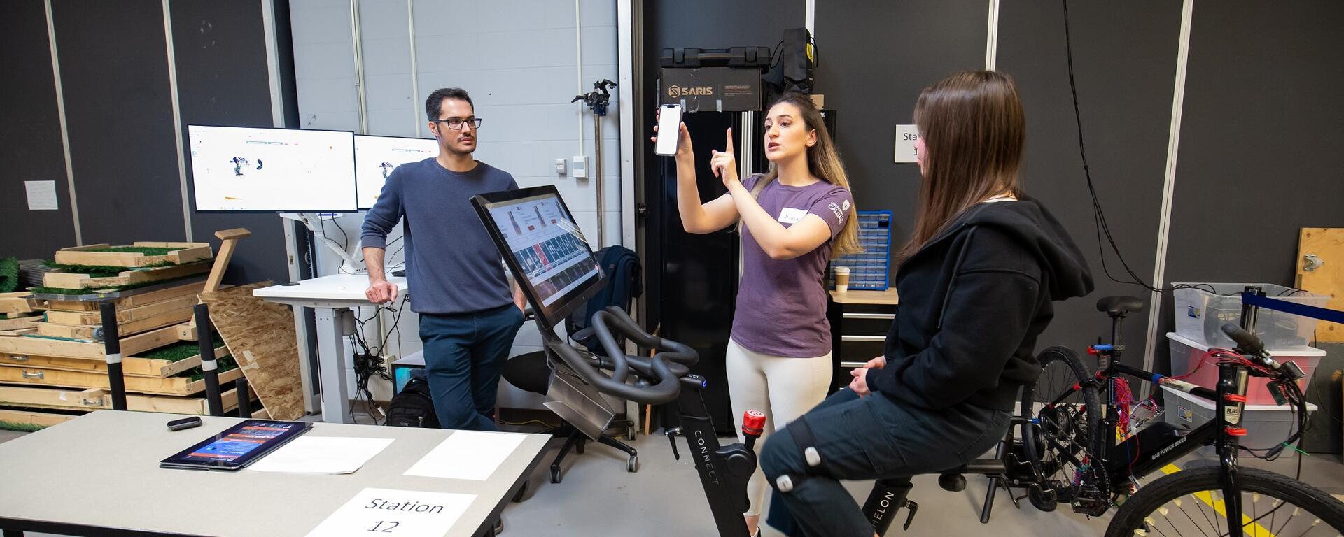 Student in the Human Performance Lab pointing at device chatting with two other students