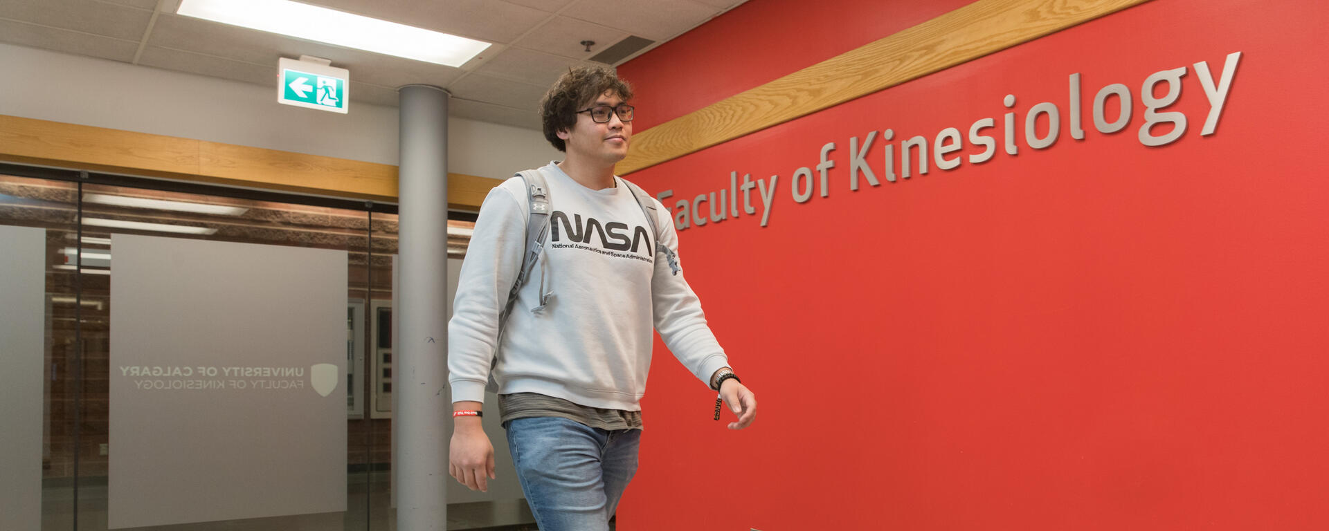 A student walking past faculty of kinesiology sign