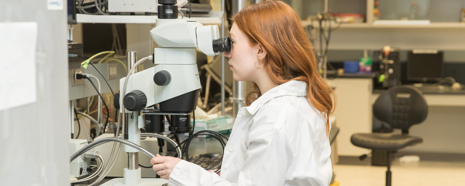 A student performing research, looking through a microscope