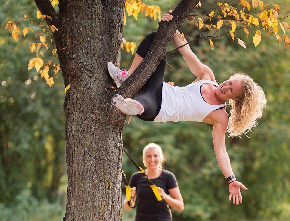 Student laughing and hanging from a tree on campus