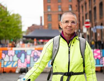 Older woman in a reflective jacket stands beside her bike looking at the camera with a small smile