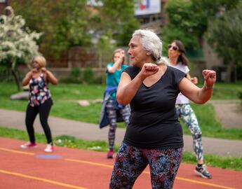 Older adults on an outdoor track pictured mid-move in a fitness class.